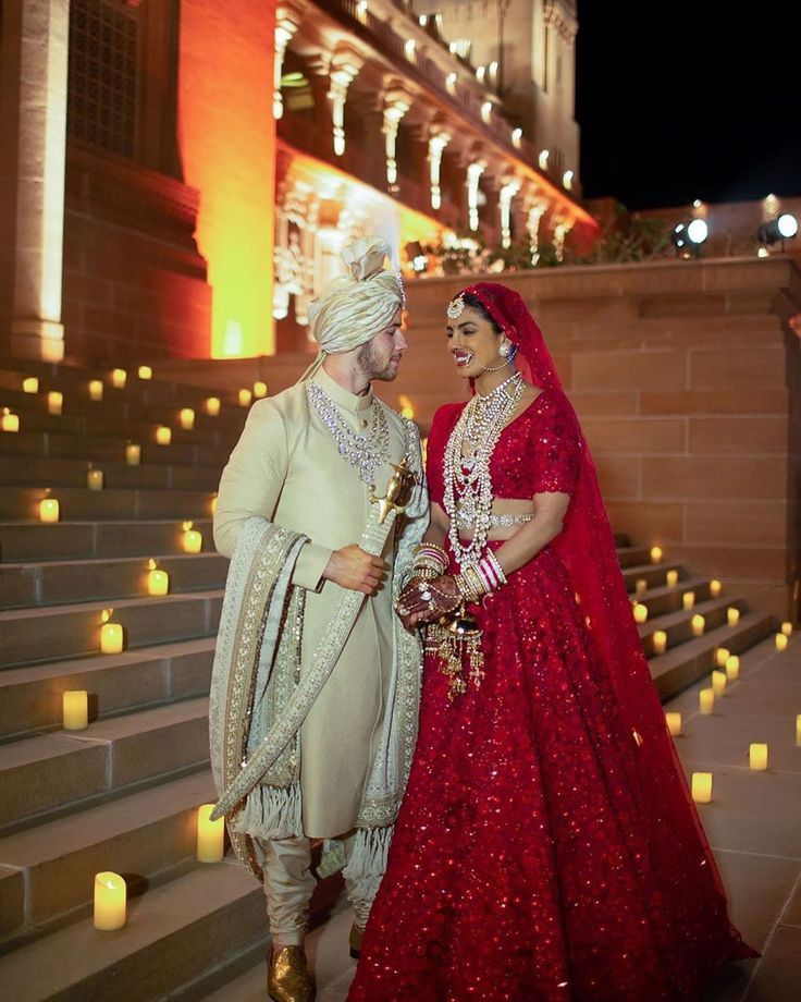 Bride and groom wearing coordinated red bridal lehenga and ivory sherwani for royal Indian wedding inspiration