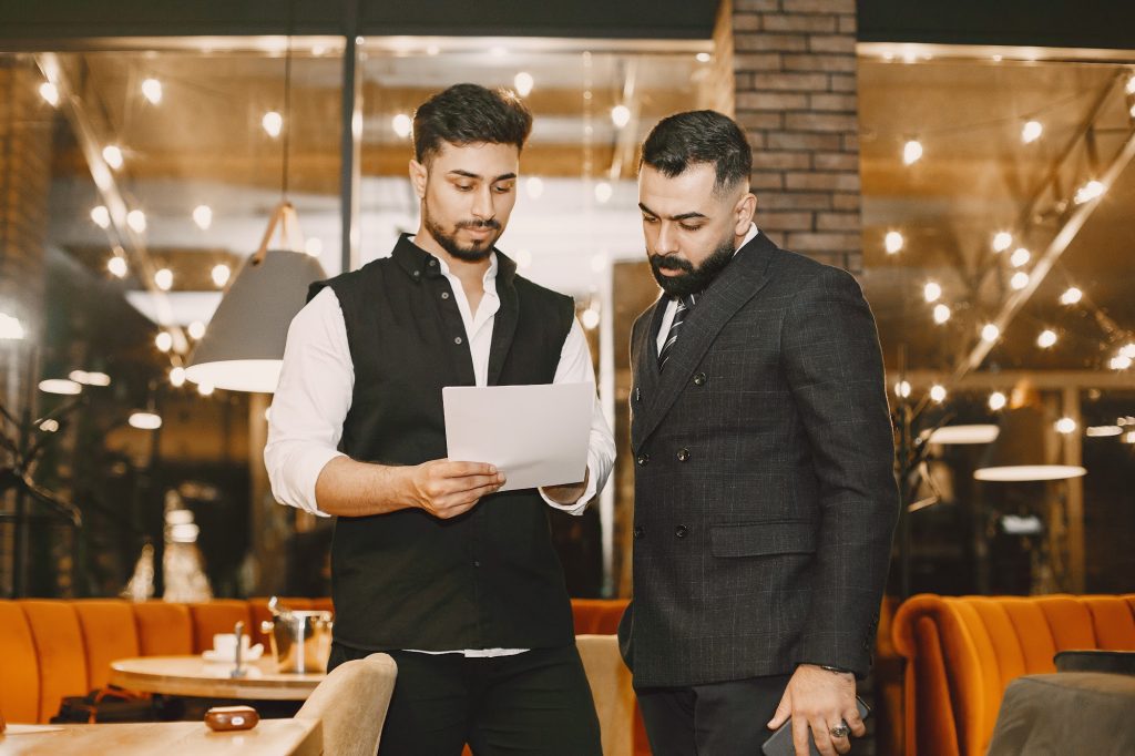 Two well-dressed men looking at a sheet of paper in a well-lit indoor cafe space